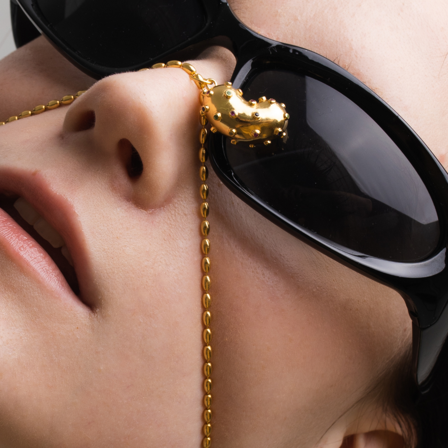 Model with black sunglasses wearing Bean pendant made of gold plated silver, natural sapphires, tsavorite and peridot