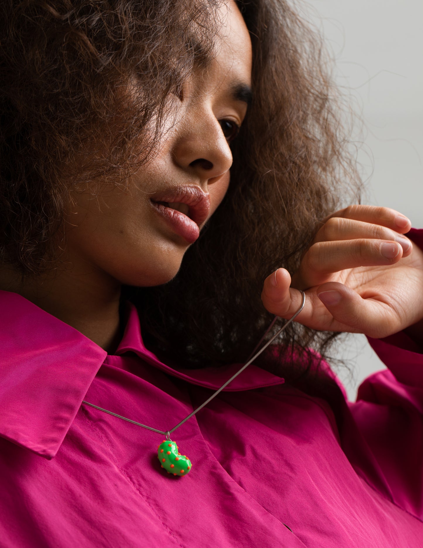 Model wearing a silver bean pendant enveloped in lush green enamel, accented with playful orange dots