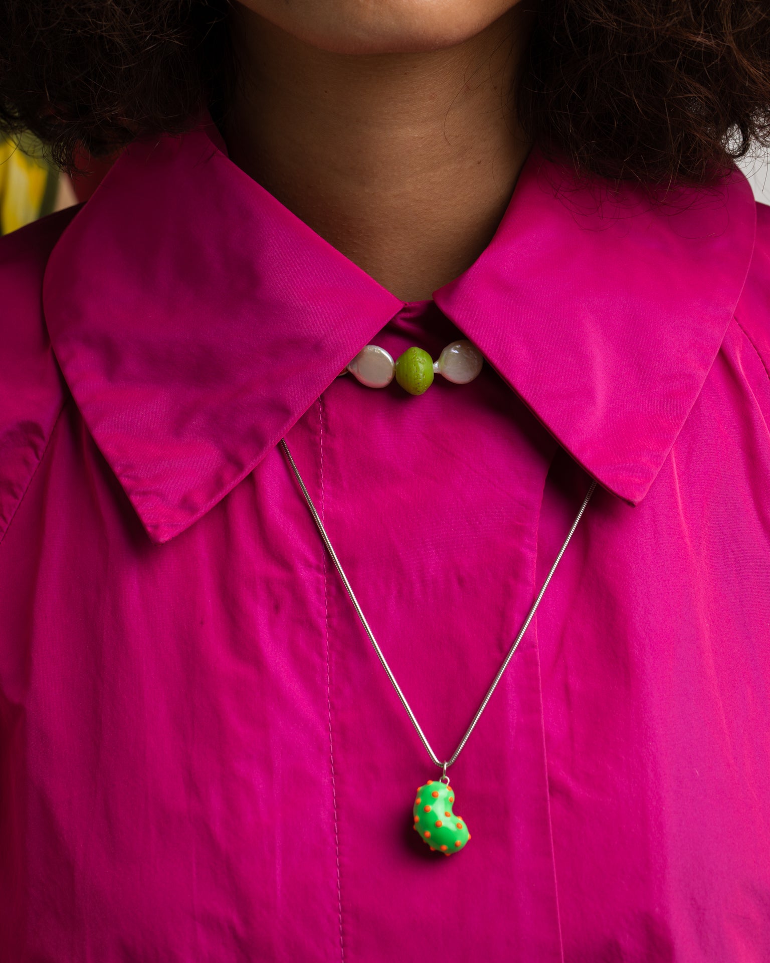 Model wearing a silver bean pendant enveloped in lush green enamel, accented with playful orange dots