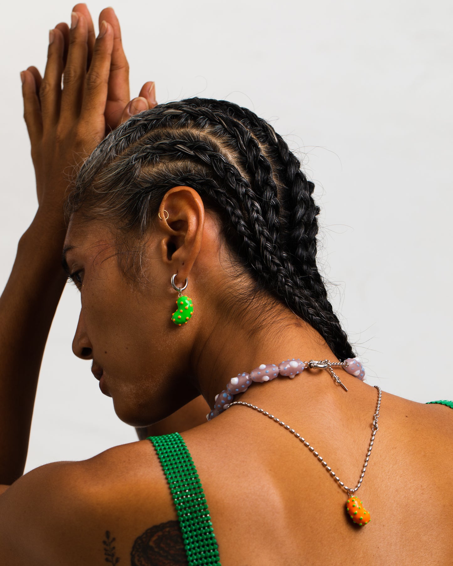 Model wearing a silver bean pendant enveloped in lush orange enamel, accented with playful green dots