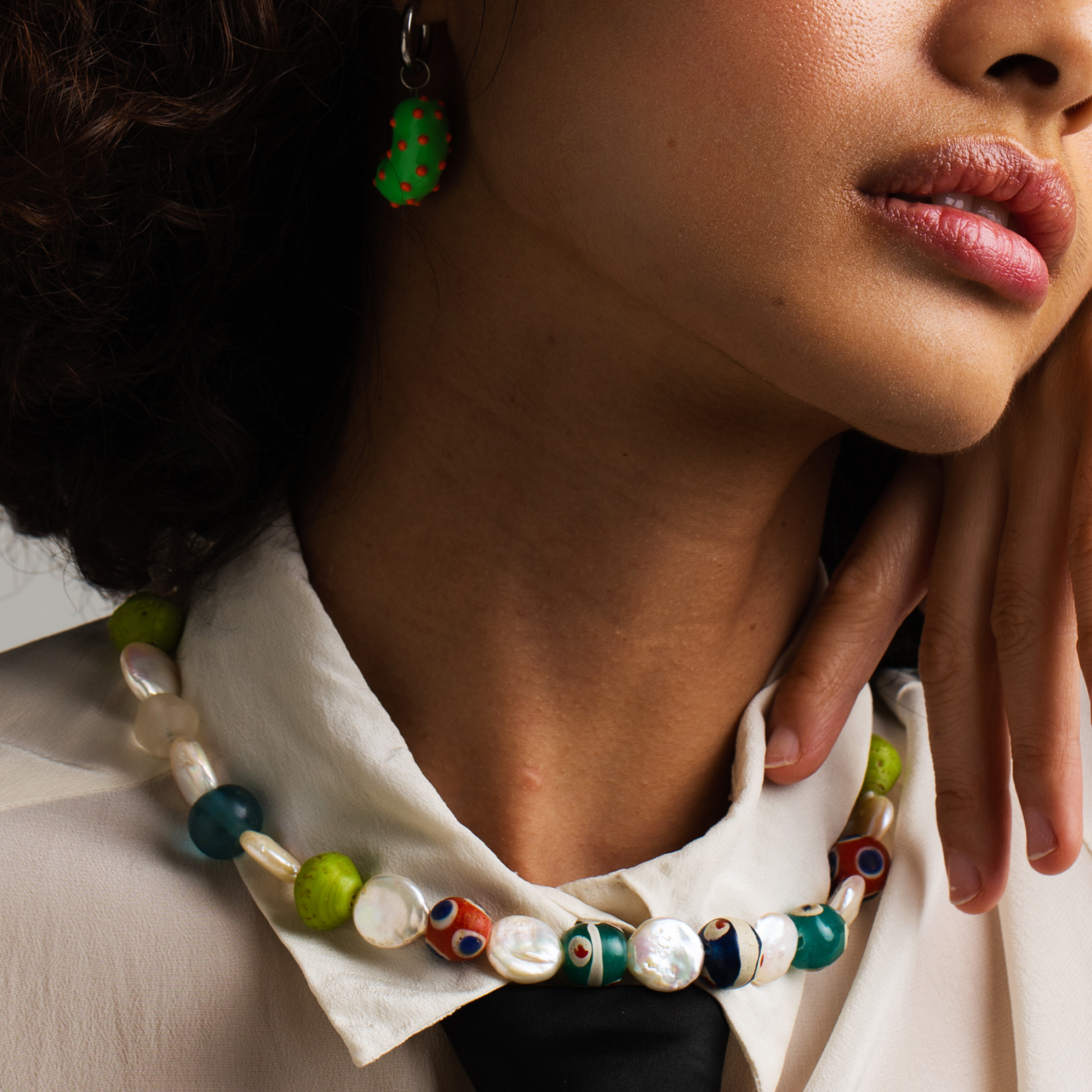 Model wearing a silver bean pendant enveloped in lush green enamel, accented with playful orange dots