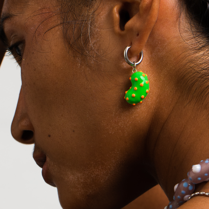 Model wearing a silver bean pendant enveloped in lush green enamel, accented with playful orange dots